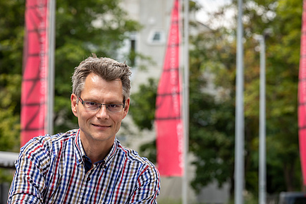 Porträt eines TU Graz-Forschers, im Hintergrund TU Graz Fahnen