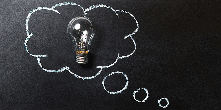 light bulb in front of a black board with a thought bubble drawn on it