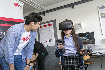 A child with virtual reality goggles on his head, next to him a young adult.