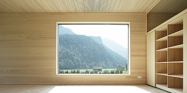 A wooden room. Centered there is a window through which you can see nature. On the right side is a cupboard.