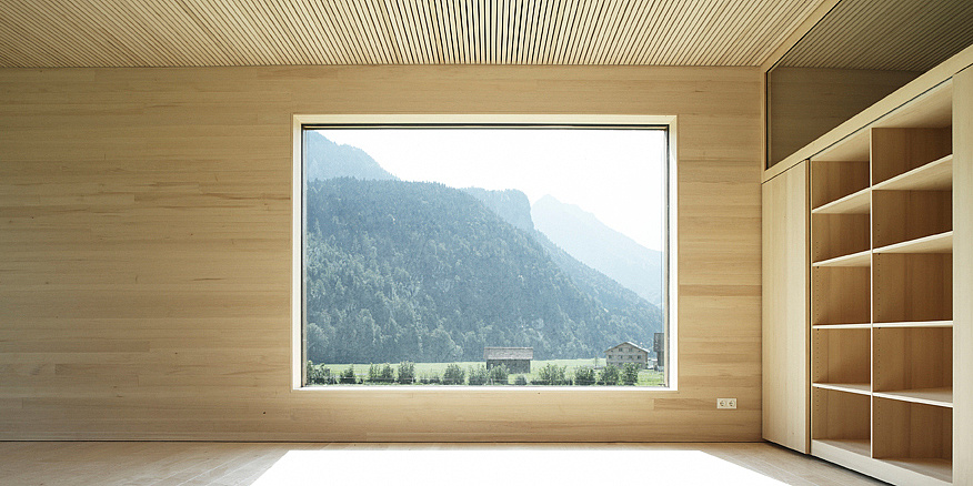 A wooden room. Centered there is a window through which you can see nature. On the right side is a cupboard.