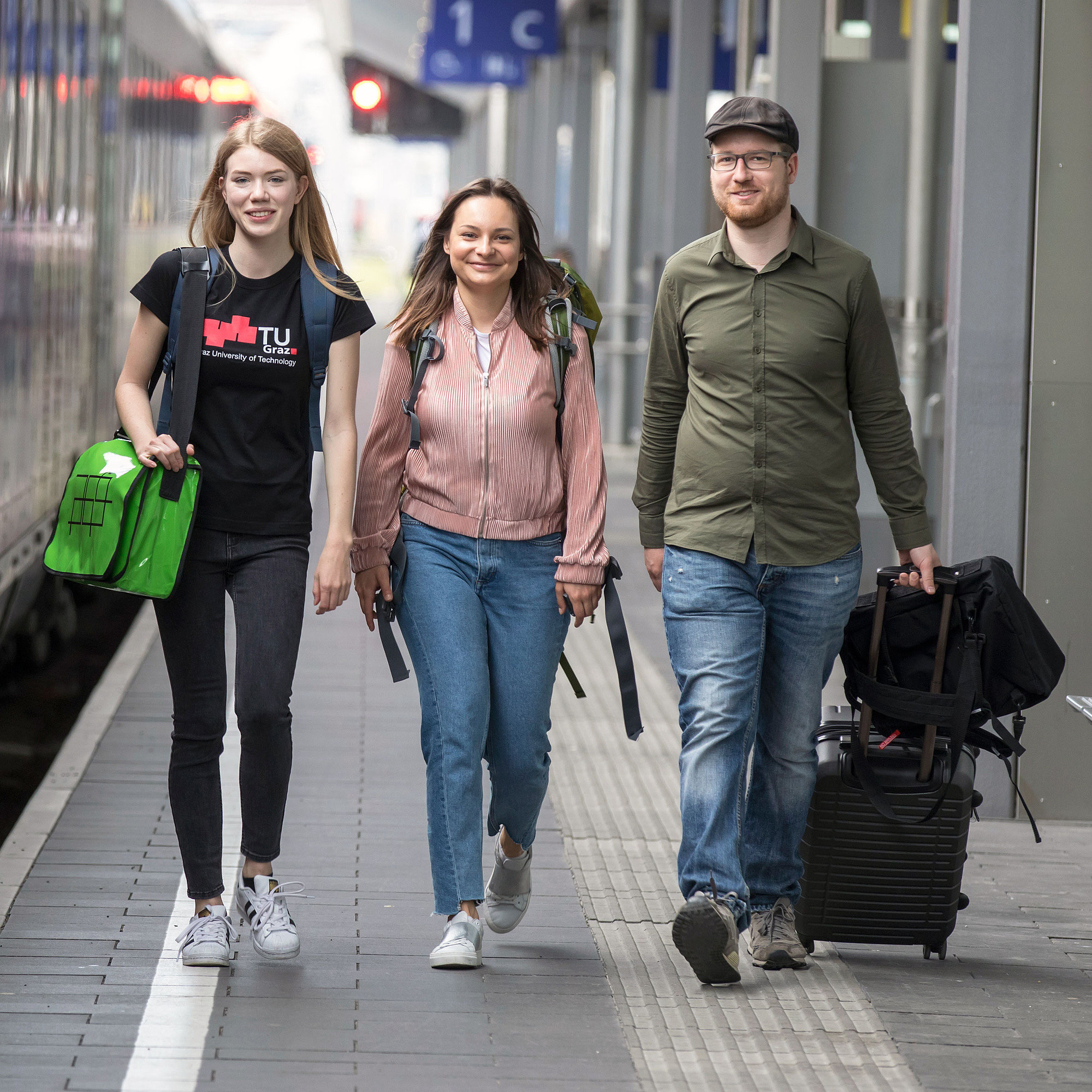 3 junge Leute mit Rucksack und Koffer am Bahnhof