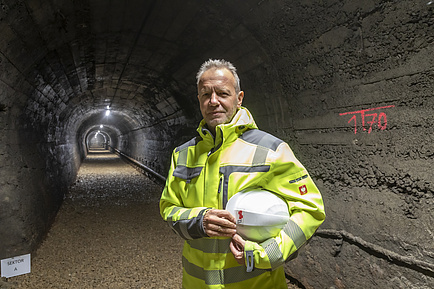 Mann mit Sicherheitsjacke und Helm unter dem Arm vor einem Tunnelportal.