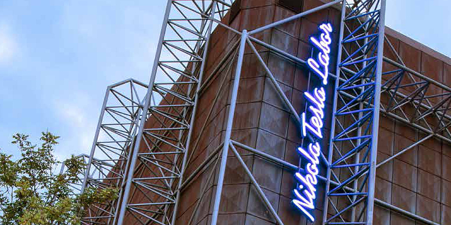 A futuristic building, in illuminated letters Nikola Tesla Labor is written vertically on the facade.