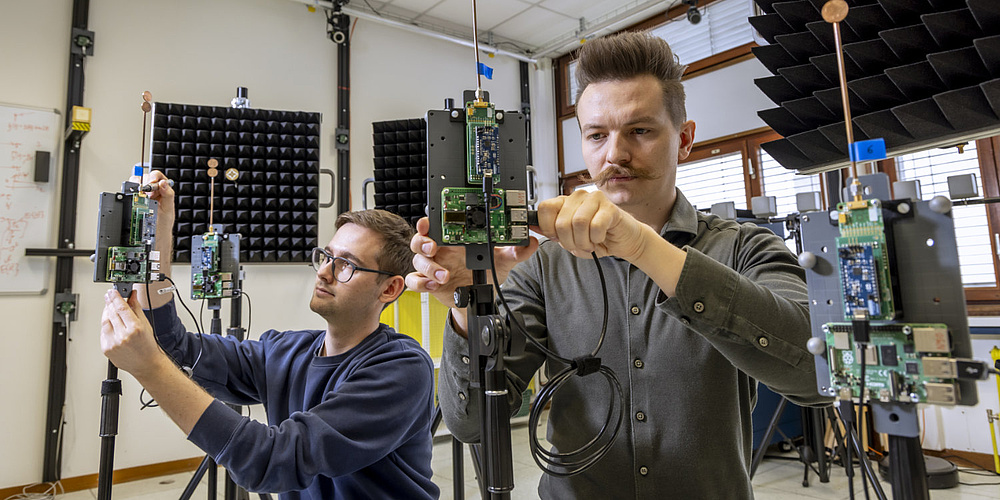 Lukas D'Angelo (left) and Benjamin Deutschmann installing IoT devices in the ultra-wideband laboratory at the Institute for Communication Networks and Satellite Communications at Graz University of Technology. Image source: Lunghammer – TU Graz Two men are assembling devices equipped with antennas and circuit boards.