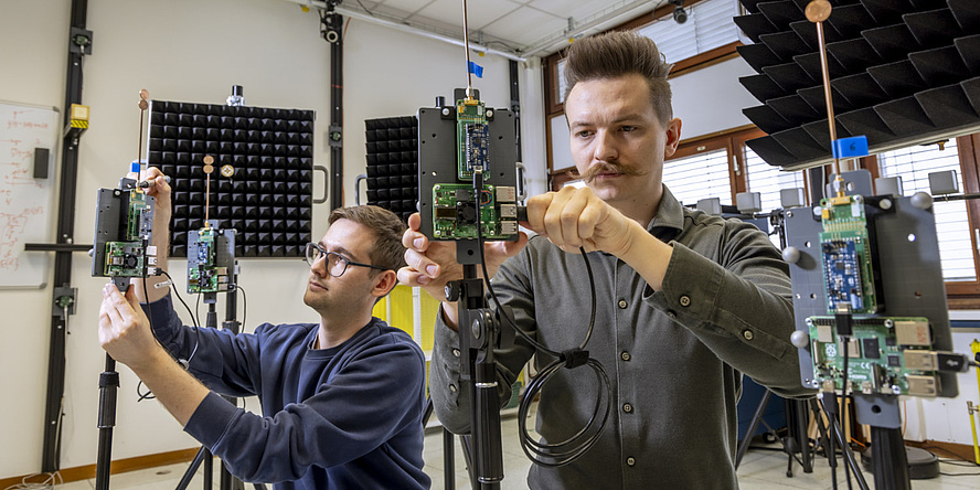 Two men are assembling devices equipped with antennas and circuit boards.