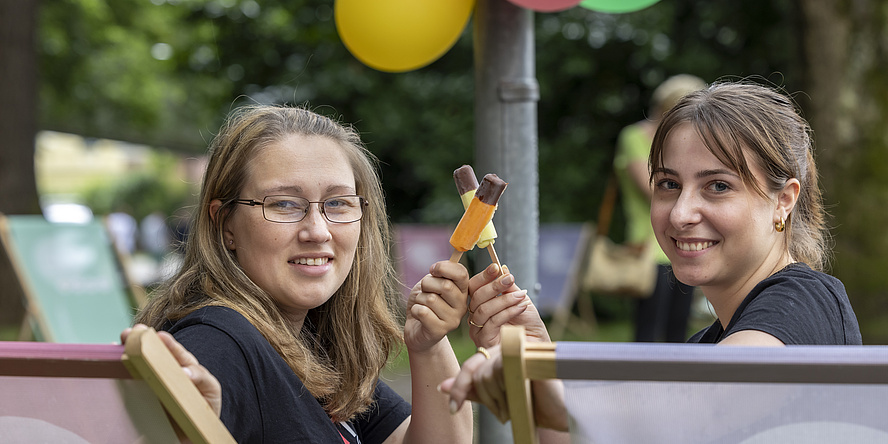 Zwei Frauen sitzen auf Liegestühlen und halten jeweils eine Twinni-Hälfte. 