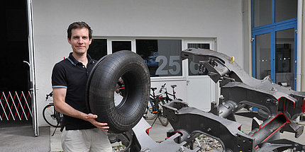 Young man with a large tyre in front of the entrance to a hall.