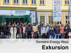 Gruppe von jungen Erwachsenen vor dem Siemens Energy Gebäude in Weiz bei sonnigem Wetter, mit Firmenlogo und Fahnen im Hintergrund, als Teil einer Exkursion.