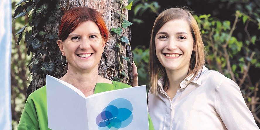 Two women are standing in front of a tree.