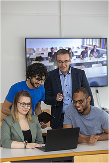 Three men and a woman look at a screen with a relaxed smile.