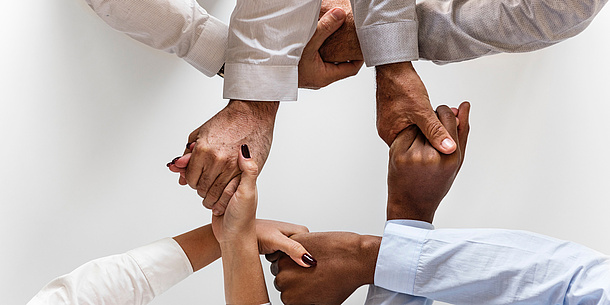 Four people shake hands, only the hands are seen in the picture. They form a square.