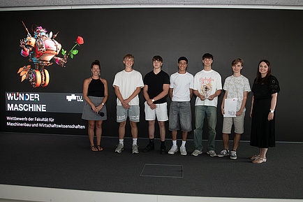 Seven people stand next to each other on a stage and smile into the camera.