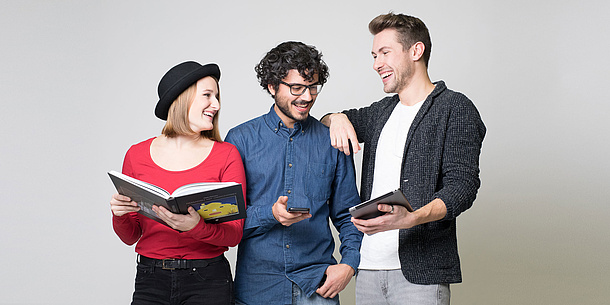3 laughing students holding a pad, a mobile phone and an iPad.