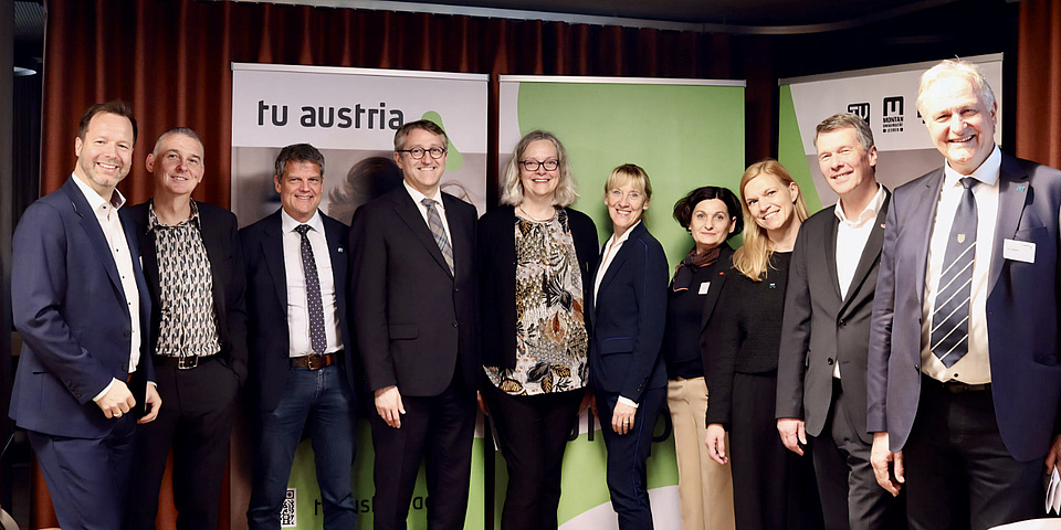 Zehn Personen stehen in einer Reihe vor einer Posterwand und schauen in die Kamera.
