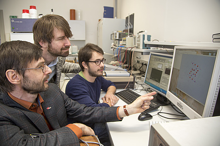Three men sit in front of a computer monitor and analyse the research results, which are displayed on the screen in the form of a graphic.