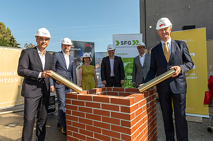 6 persons with construction helmet and foundation stone rolls in front of a small wall