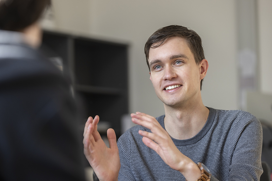 Mann mit kurzen braunen Haaren in einem Interview. Er spricht gerade und gestikuliert. 