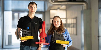 A young man and a young woman proudly show rocket-shaped trophies from competitions.