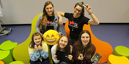 Vier Mädchen im Alter von 10 bis 14 Jahren und eine Frau mit Brille präsentieren jeweils eine Computerplatine, ein Tablet und einen drei Zentimeter großen kugelförmigen Roboter.
