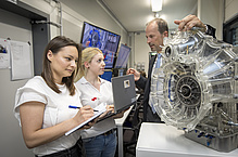 Two women and a man with a big machine part.