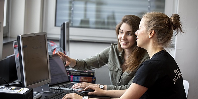 Zwei Personen sitzen vor einem Computer.