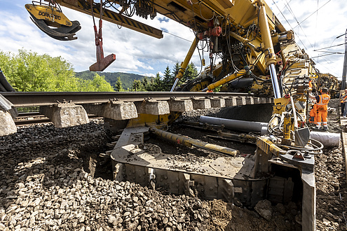 Ausschnitt einer Baumaschine auf Schienen, die ein Stück eines Gleiskörpers anhebt.