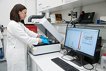 A woman in a lab coat places material samples into an open measuring device.