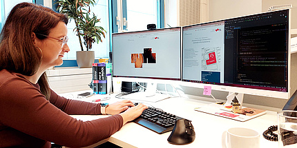Eine Frau sitzt am Arbeitsplatz vor zwei Bildschirmen und programmiert