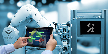 A person operates the arm of an industrial robot via a tablet.