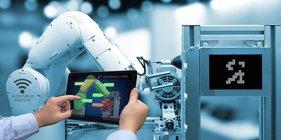 A person operates the arm of an industrial robot via a tablet.