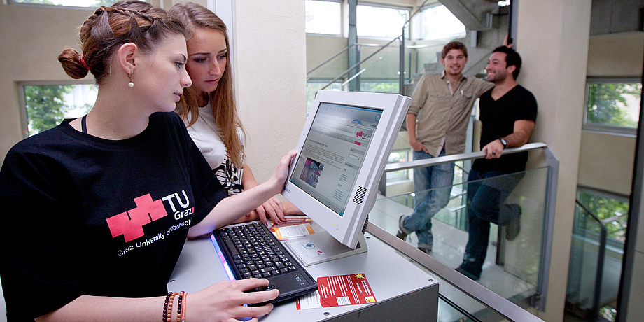 Junge Frau bei der Computereingabe, eine Kollegin blickt ihr über die Schulter.