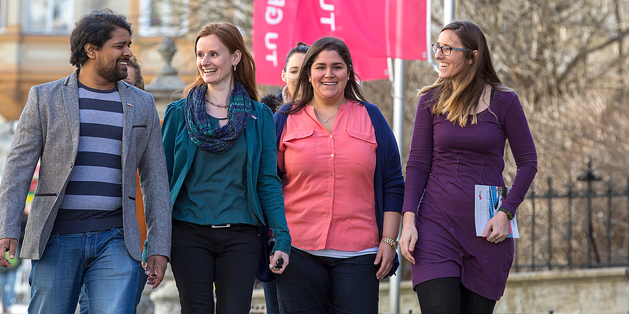 Four staff members of different origin (three female, one male) on campus "Alte Technik" of TU Graz.