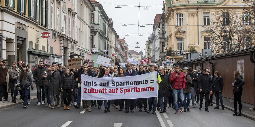 Several people are walking on a street holding a banner.