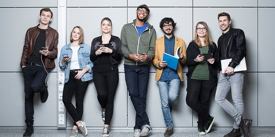 Die „Faces“ der TU Graz Lukas, Benedict, Johanna, Sara, Leonardo, Verena, Lukas von links nach rechts vor einer großgefliesten Wand am Campus der TU Graz.