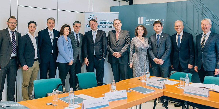 a group of eleven people in front of an Alpe Adria university branded background