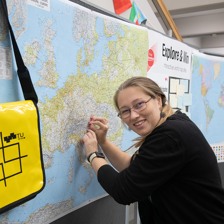person standing next to a world map putting a pin on the map 