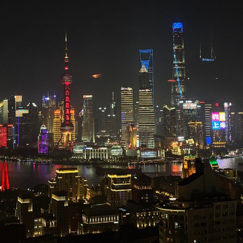 Skyline von Shanghai bei Nacht: Zahlreiche Wolkenkratzer hell erleuchtet, umgeben von einem dunklen breiten Fluss, der die Stadt in zwei Teile teilt.