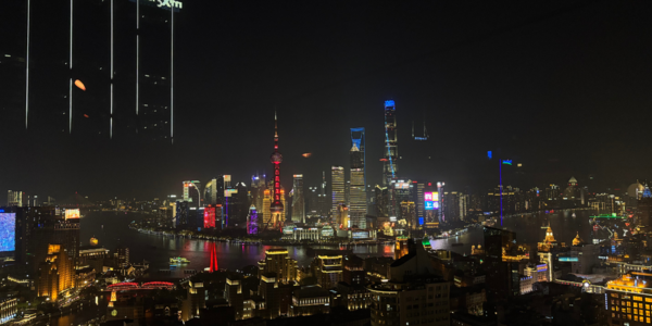 Skyline von Shanghai bei Nacht: Zahlreiche Wolkenkratzer hell erleuchtet, umgeben von einem dunklen breiten Fluss, der die Stadt in zwei Teile teilt.