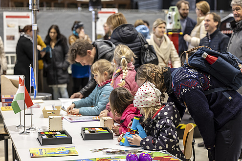 Children and adults are busy experimenting at several tables.