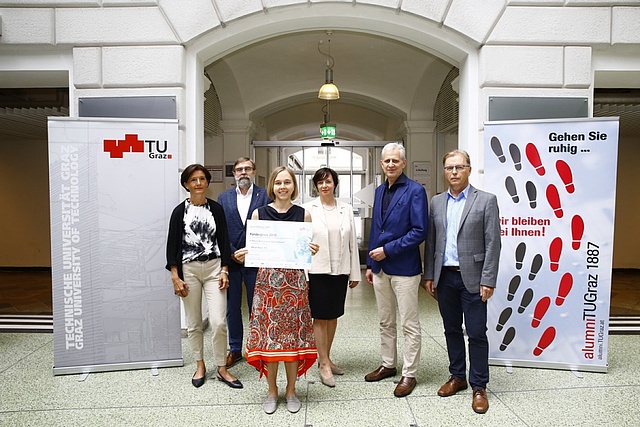 Miriam Bayer is surrounded from TU Representatives and is holding the printed award in her hand