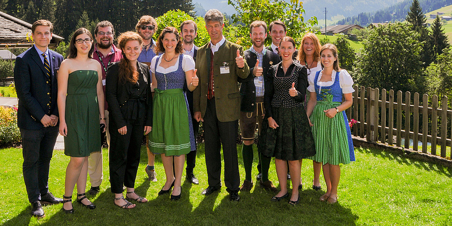 A group of young people are standing on a lawn. In their midst the rector of TU Graz