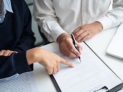 Two persons sitting next to each other pointing on a document.