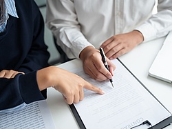 Two persons sitting next to each other pointing on a document.