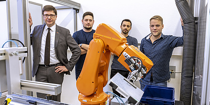 Mehrere Männer stehen hinter einem orangen Roboterarm.