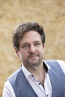 A man wearing a waistcoat looks into the camera.