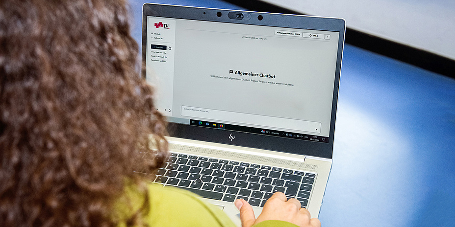 Eine Frau blickt auf einen Laptop-Bildschirm. Dieser zeigt das TU Graz-Logo, den Schriftzug „Allgemeiner Chatbot“ und ein Chatfenster.