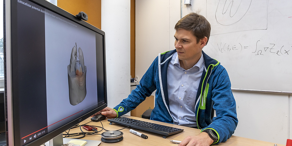 A man sitting at a desk and looking at a computer monitor which shows a computer generated image of a human heart