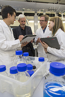 Three men and a woman in conversation, many transparent bottles with blue screw caps in front of them.