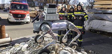 Spürroboter mit vier großen Rädern, Sensoren und Kameras auf einem Geröllhügel bei einer Feuerwehrübung.